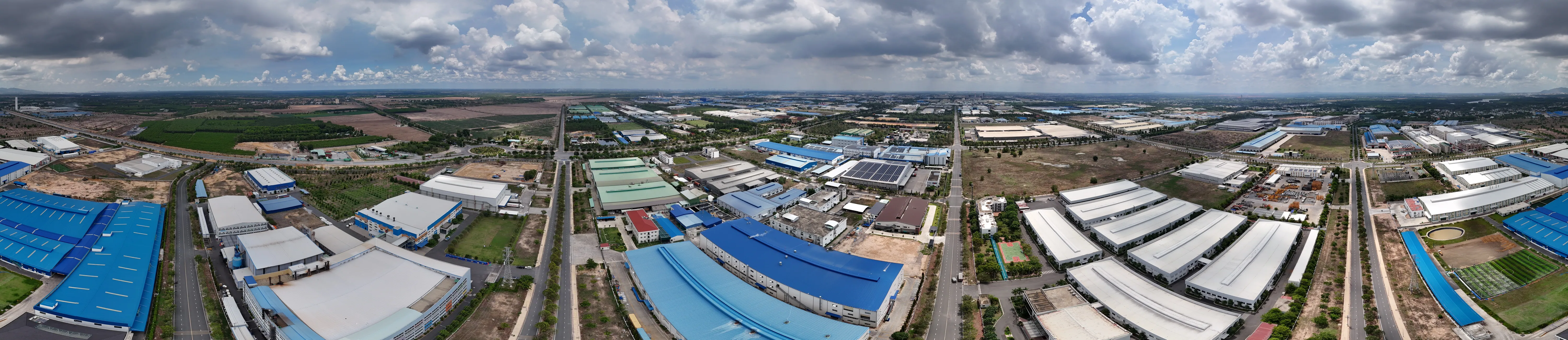 Ảnh toàn cảnh Khu công nghiệp Nhơn Trạch 6 chụp từ trên cao: đường nội bộ chạy thẳng về phía chân trời dưới trời nhiều mây, hai bên là các nhà xưởng mái tôn xanh và trắng, một số mái đã lắp tấm pin điện mặt trời, xen giữa là dải cây xanh cách ly và các lô đất đã xây dựng